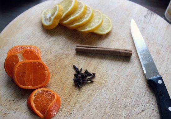 Sliced orange and lemon on a wooden chopping board, next to cinnamon sticks and star anise.