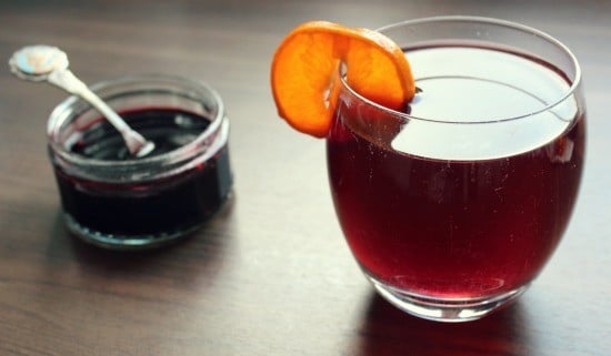 Glass filled with a drink and slice of orange, next to a bowl of syrup.