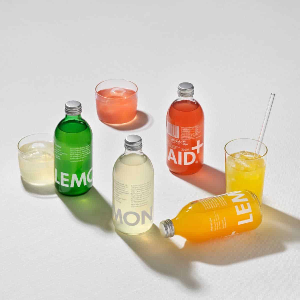 Four bottles of Lemonaid soft drinks, next to three full glasses.