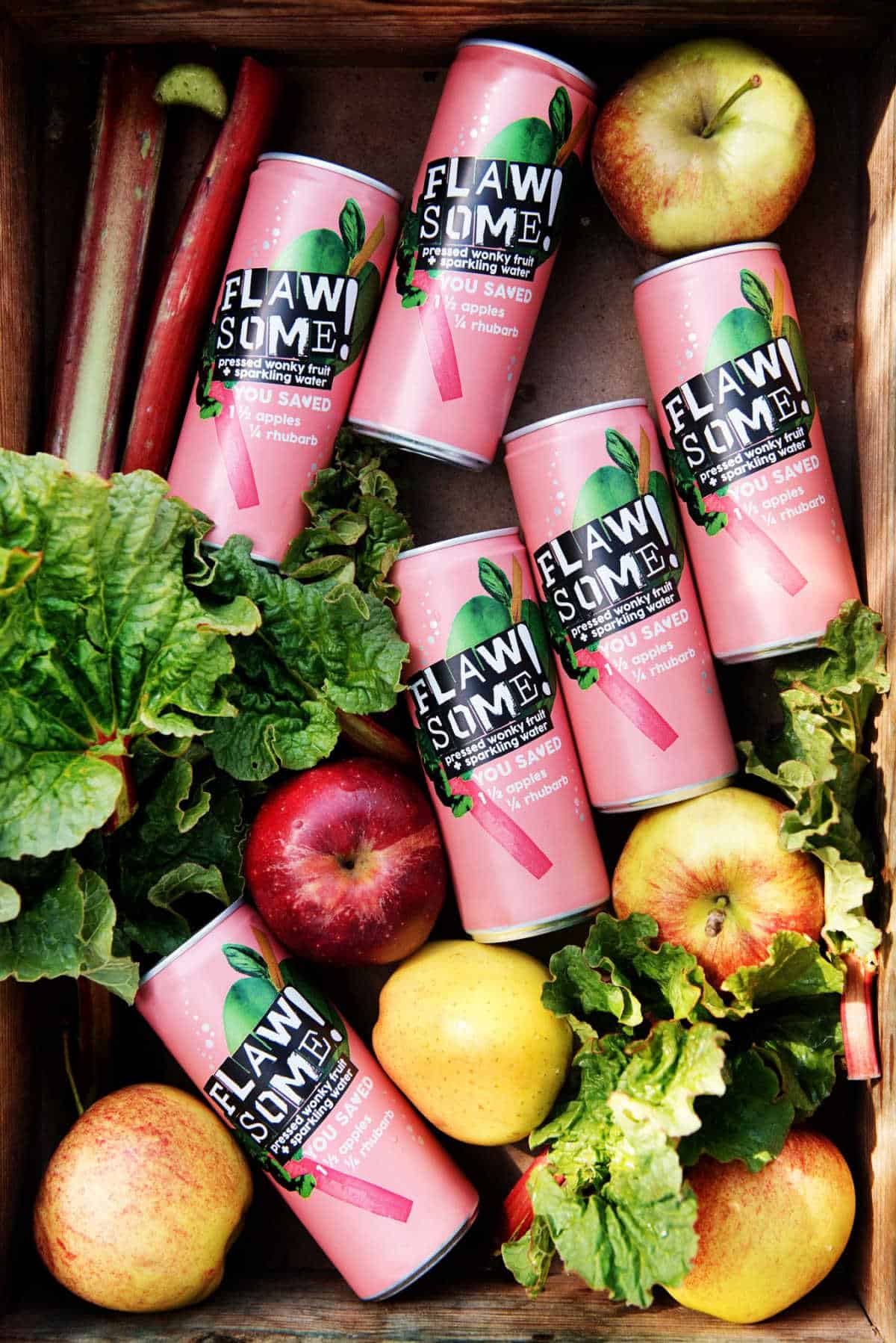 Can of Flawsome rhubarb and apple sparkling water in a box with fresh rhubarb and apple.