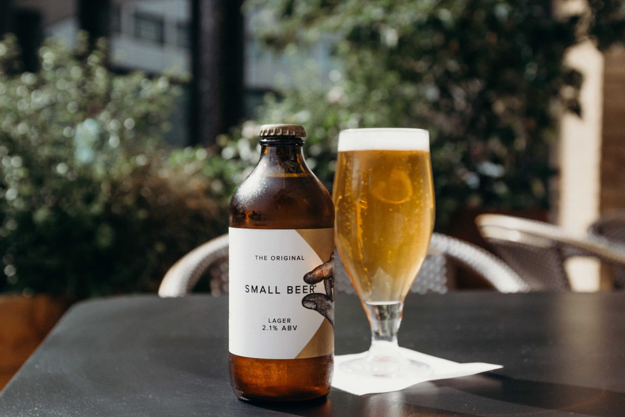 Botle of small beer on an outdoor table, next to a glass full of ale.