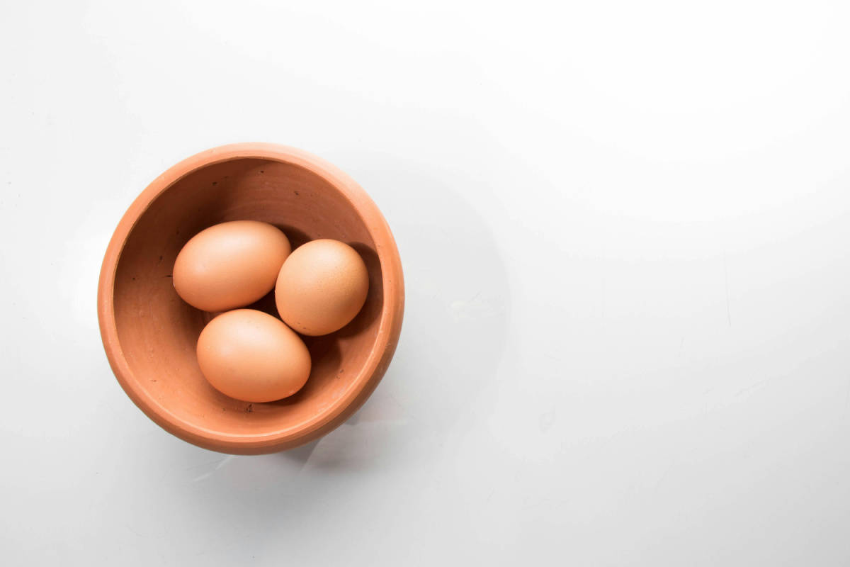 Three eggs in a wooden bowl on a white table.